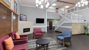 A spacious living area with a fireplace, a staircase, and a flat-screen TV mounted on the wall. - AmericInn by Wyndham Grinnell (Grinnell)