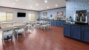 A dining area with wooden tables and chairs, a kitchen counter with appliances, and a blue brick backsplash. - AmericInn by Wyndham Grinnell (Grinnell)