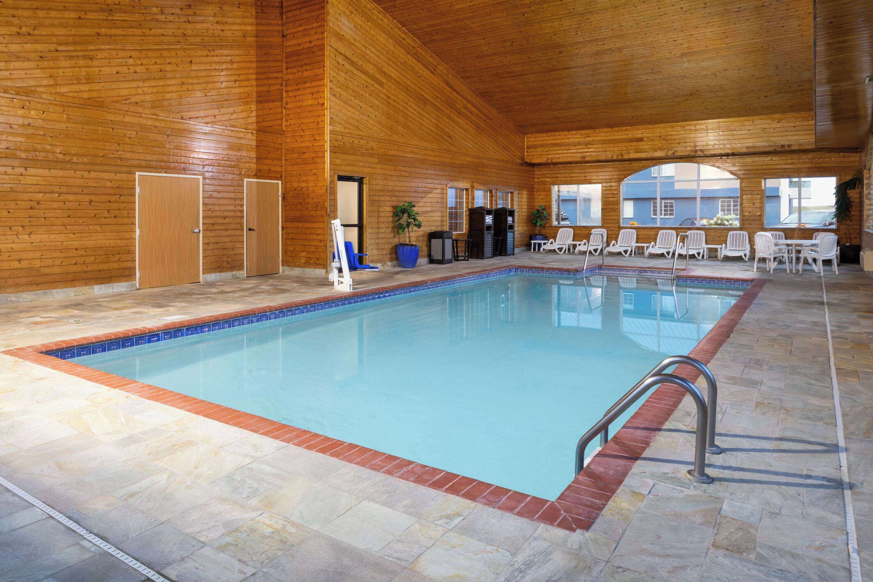An indoor swimming pool with a wooden interior, tiled floor, and several lounge chairs.