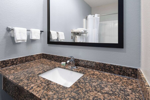 Un baño con lavamanos de encimera de granito, un espejo y toallas blancas en un perchero.