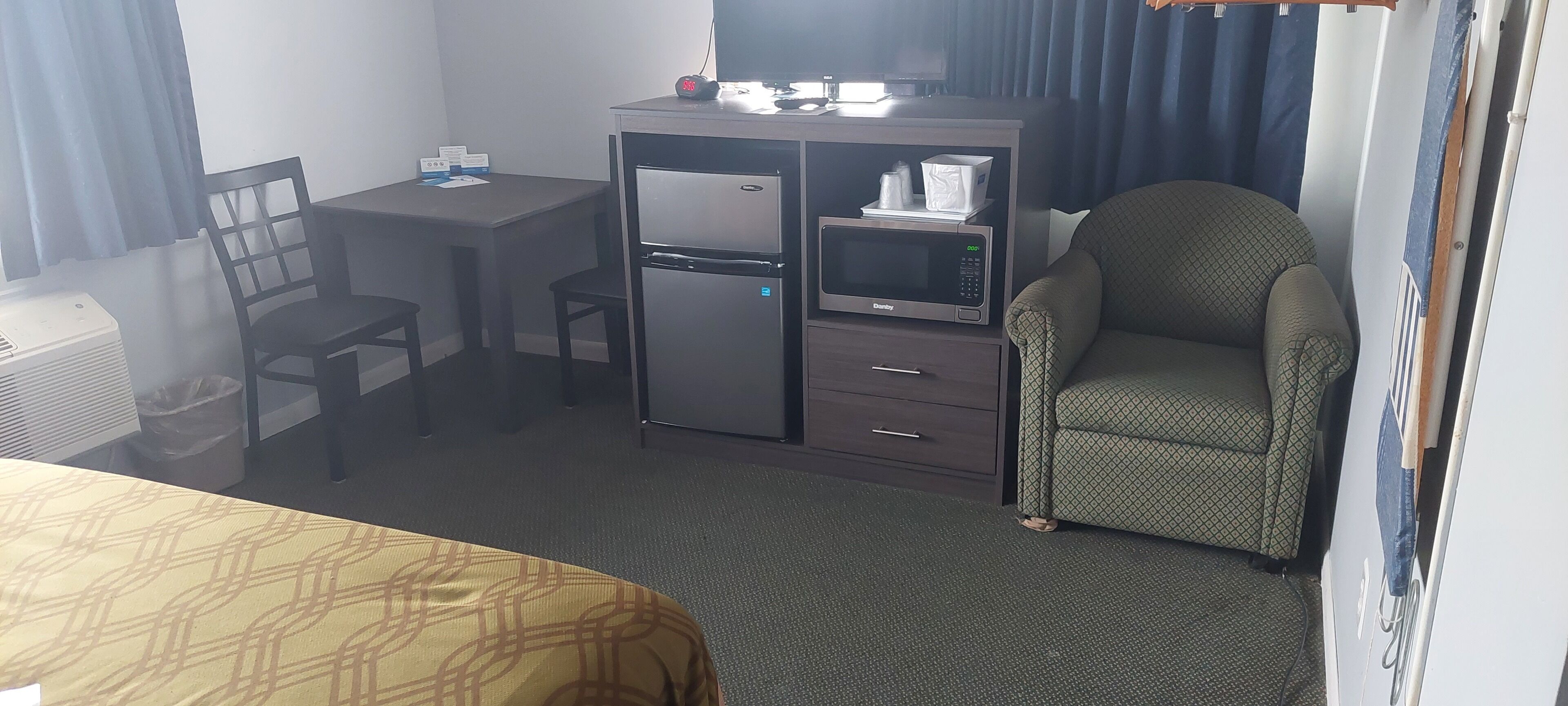 A hotel room with a bed, a desk with a computer, a refrigerator, a microwave, and a chair.