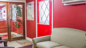 Una habitación con paredes rojas, un sofá beige con estampado, una silla de madera y una planta en maceta.