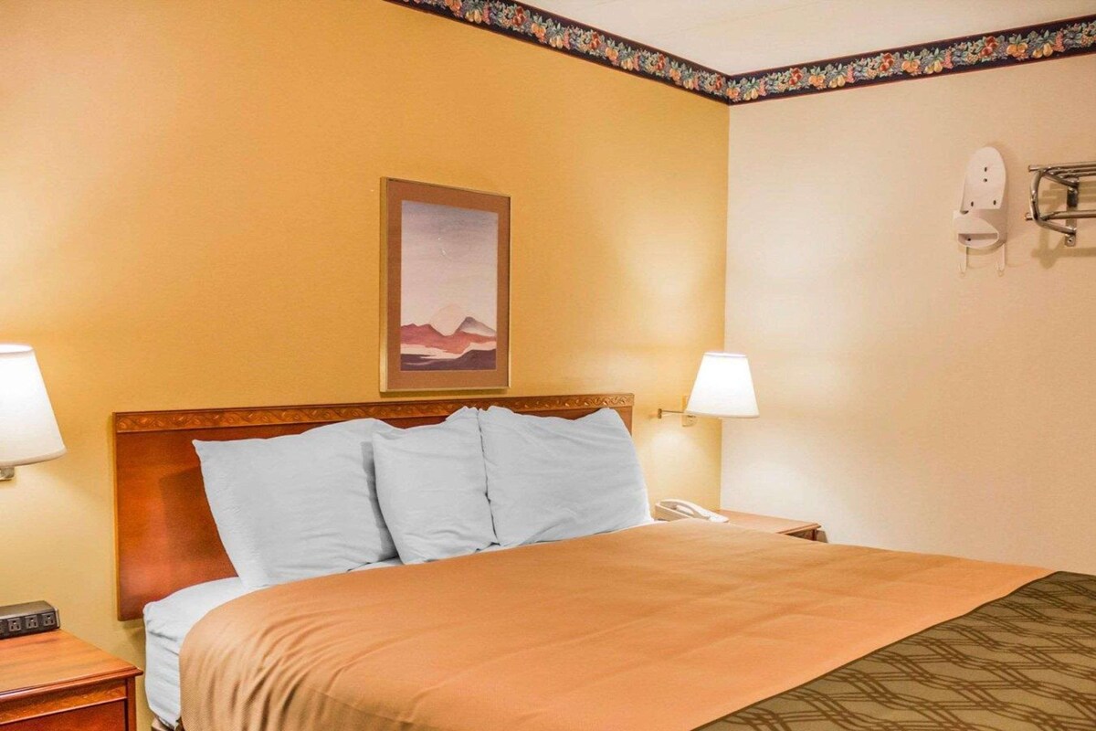 A hotel room with a bed, two bedside lamps, a nightstand, a telephone, and a framed picture on the wall.