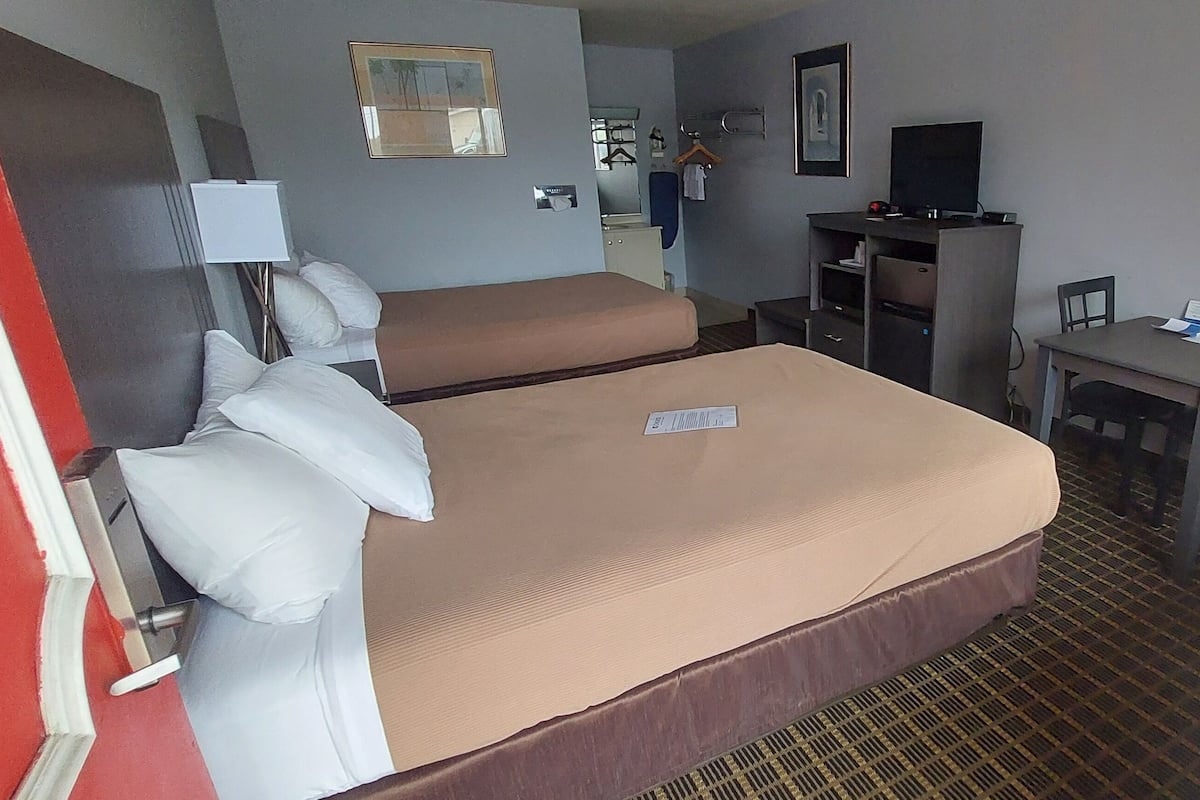 A hotel room with two beds, a desk, a chair, a television, and a painting on the wall.