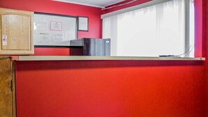 Una habitación con paredes rojas, un armario de madera, un certificado enmarcado y una ventana con cortinas.