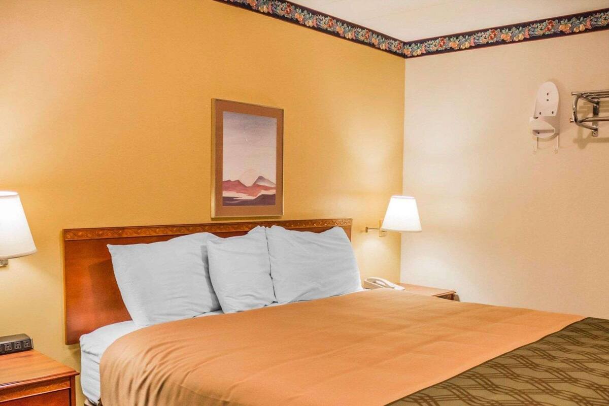 A hotel room with a bed, two bedside lamps, a nightstand, a telephone, and a framed picture on the wall.