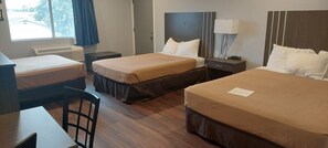 A hotel room with three beds, a desk, and a chair. - Rodeway Inn Kalkaska (Kalkaska)