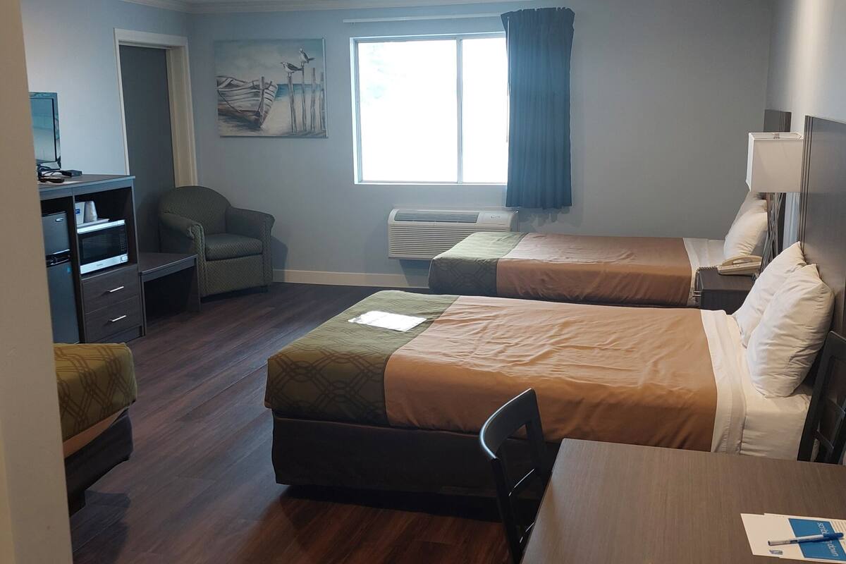 A hotel room with two beds, a desk, a chair, a TV, a chair, a window with curtains, and a painting on the wall.