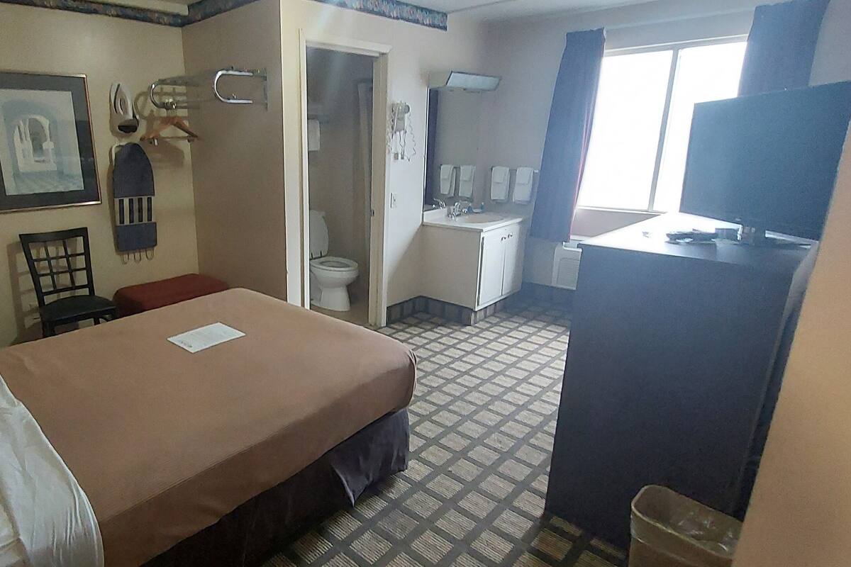 A hotel room with a bed, a desk, a chair, a small table, a TV, a bathroom, and a window.
