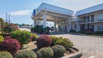A motel with a gas station, featuring a covered parking area, a two-story building with a balcony, and landscaped gardens.