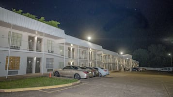 Un motel con varias habitaciones, un estacionamiento y algunos coches aparcados al frente.