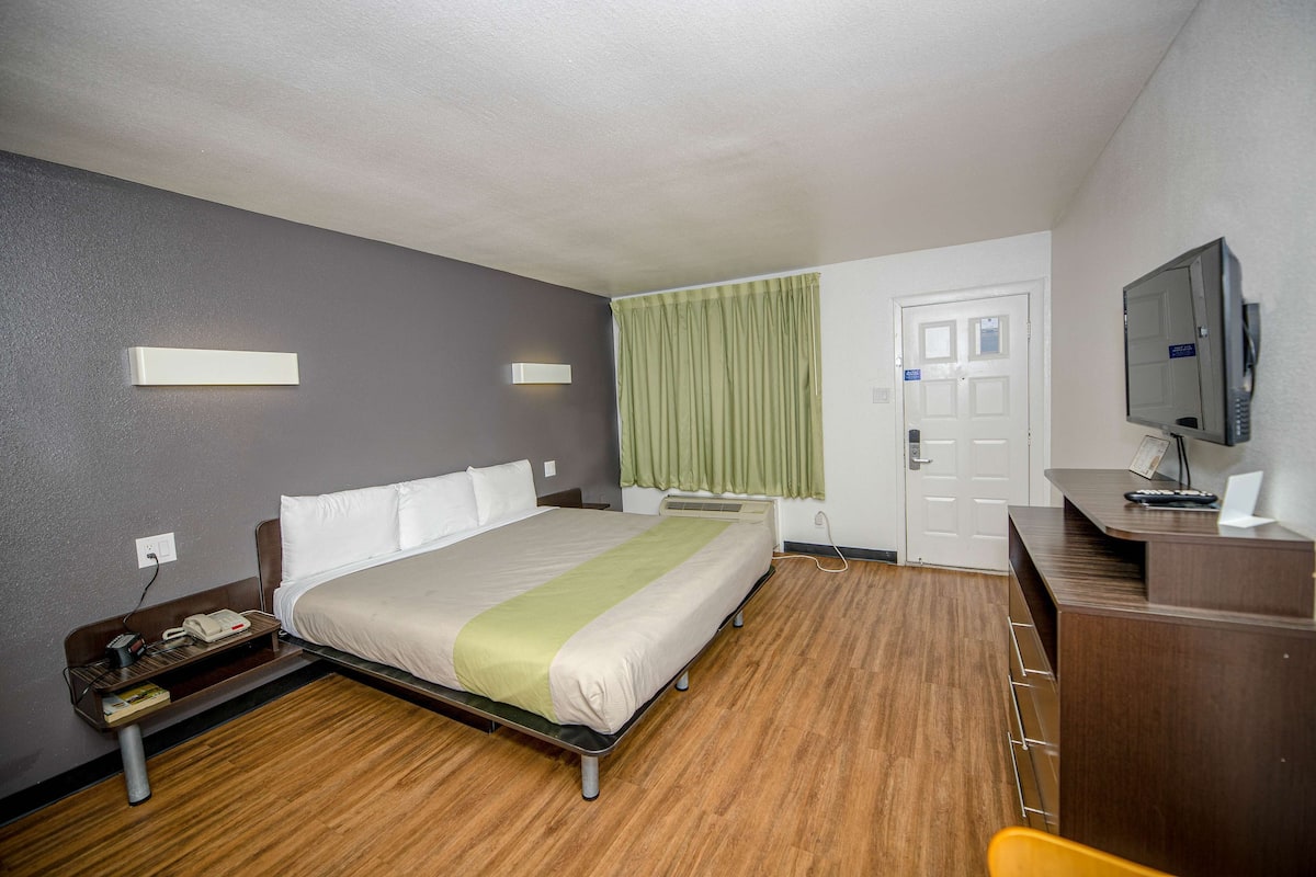 A hotel room with a bed, bedside table, desk, chair, and a television.