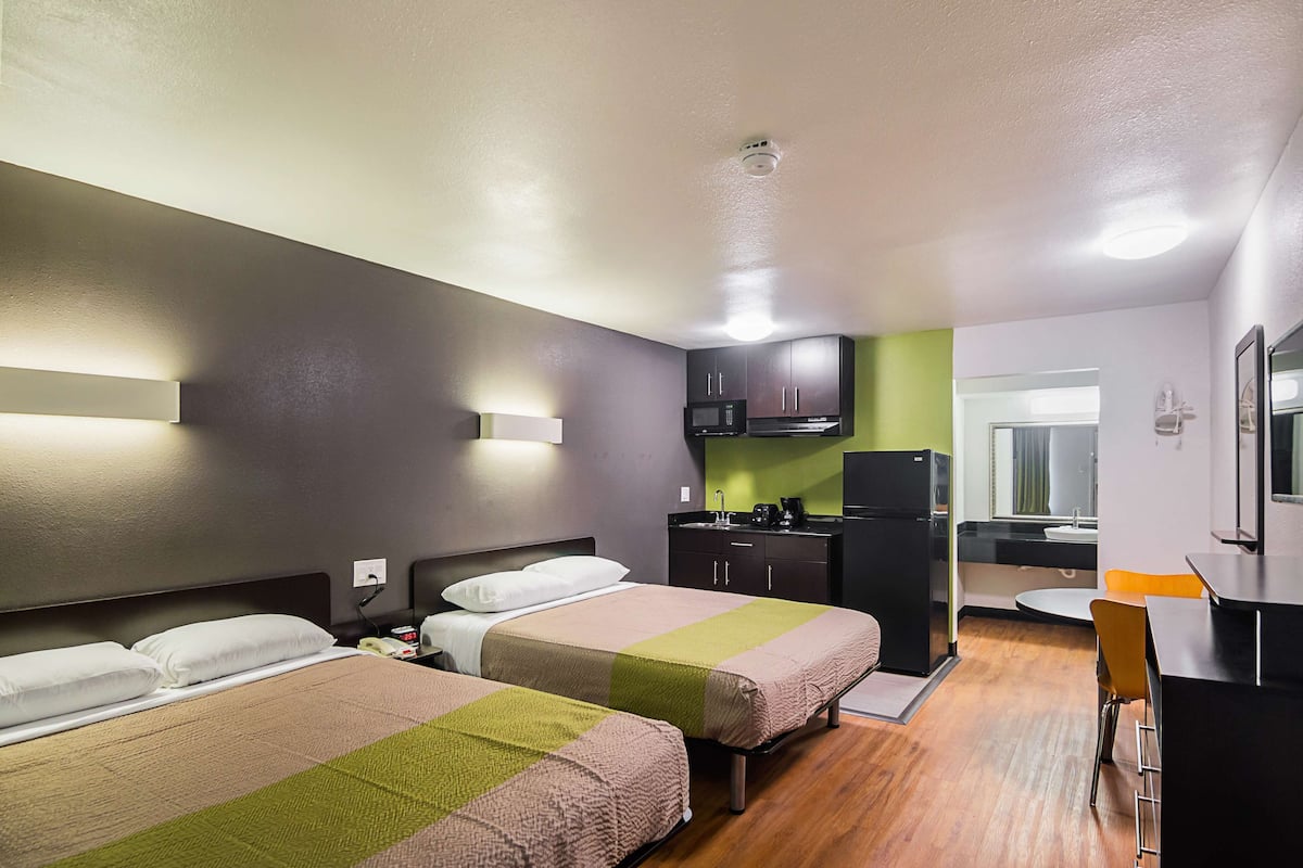 A hotel room with two beds, a kitchenette, a dining area, and a bathroom.