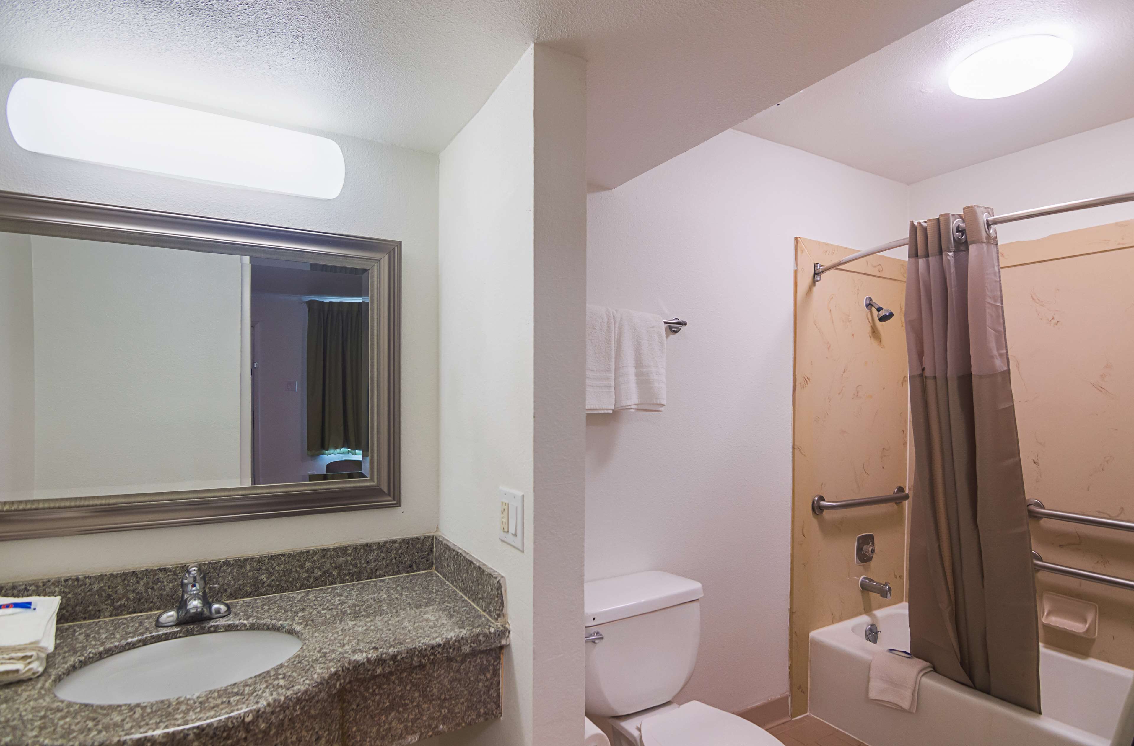 A bathroom with a granite sink, a toilet, and a shower with a grab bar.