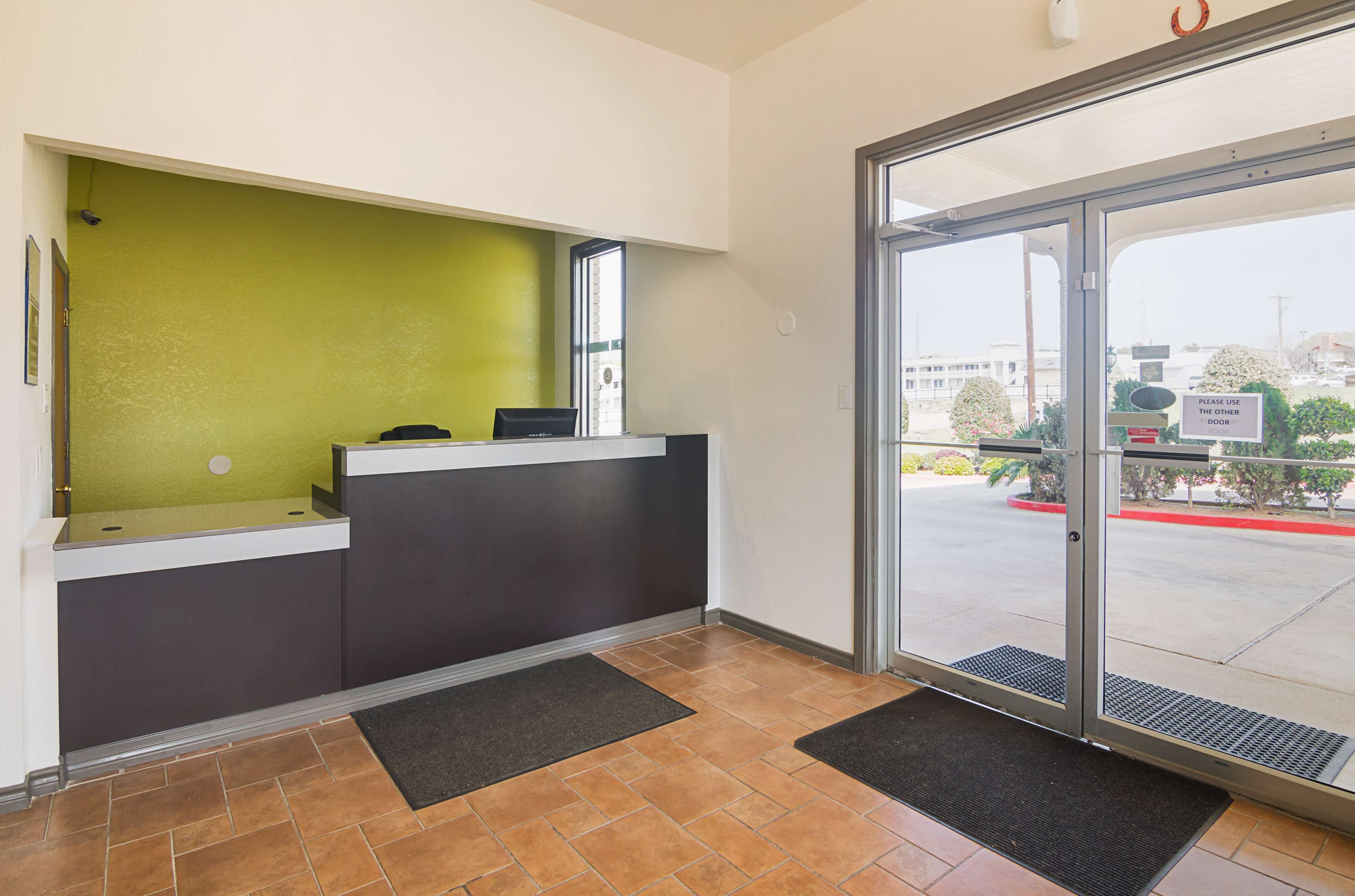 A reception area with a green wall, a reception desk, and a glass door leading outside.