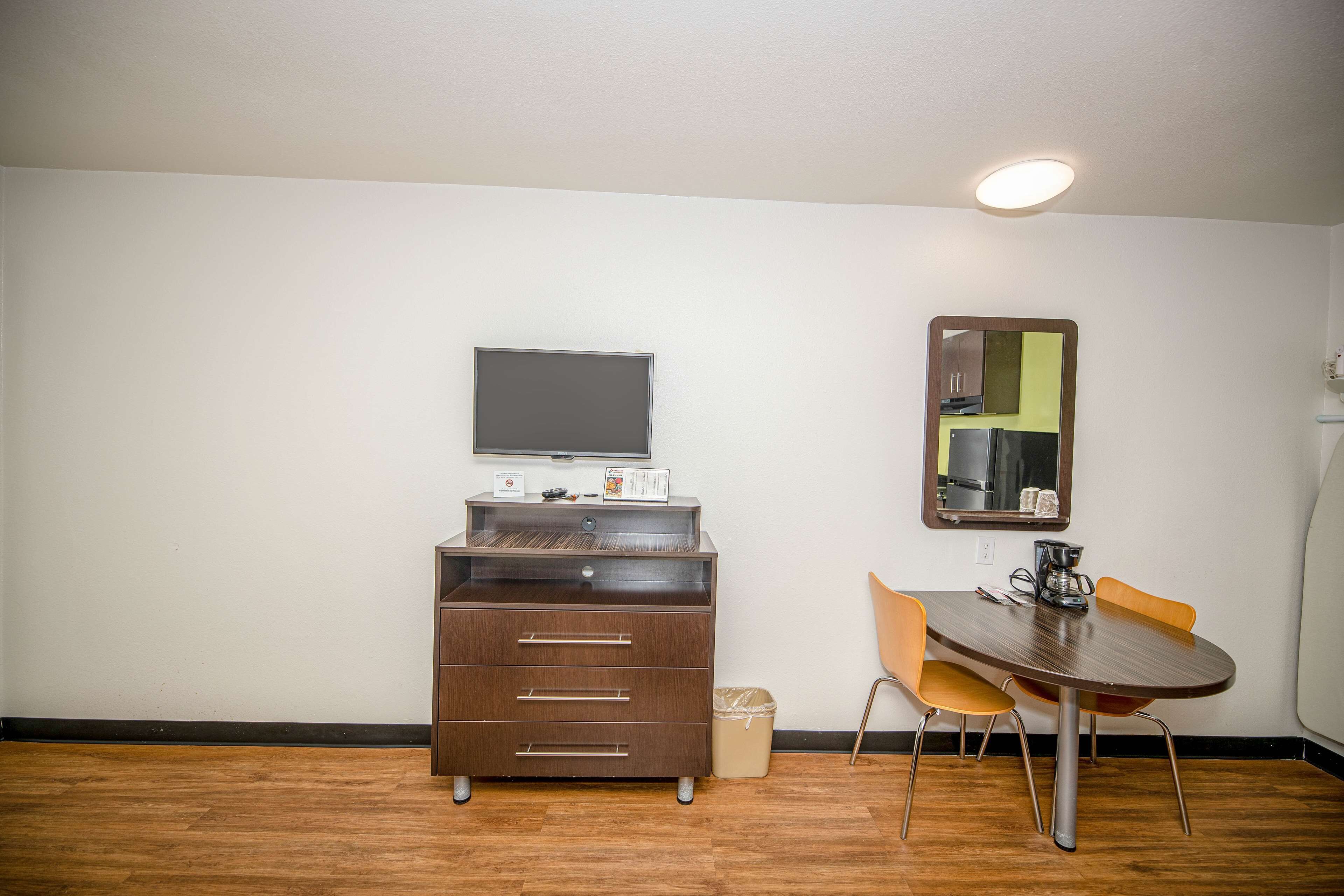 A small room with a wooden cabinet, a flat-screen TV, a mirror, and a dining table with two chairs.