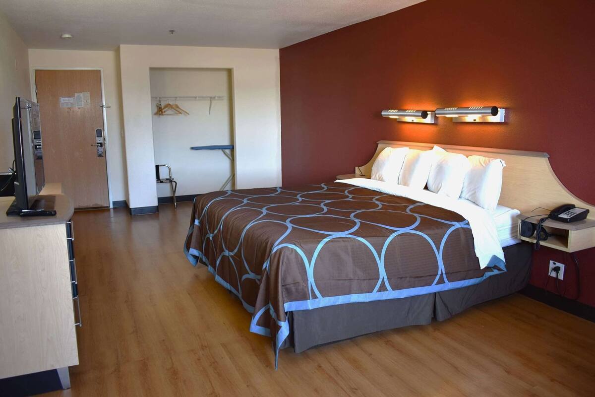 Een hotelkamer met een bed, nachtkastje, lamp en een bureau met een computer.