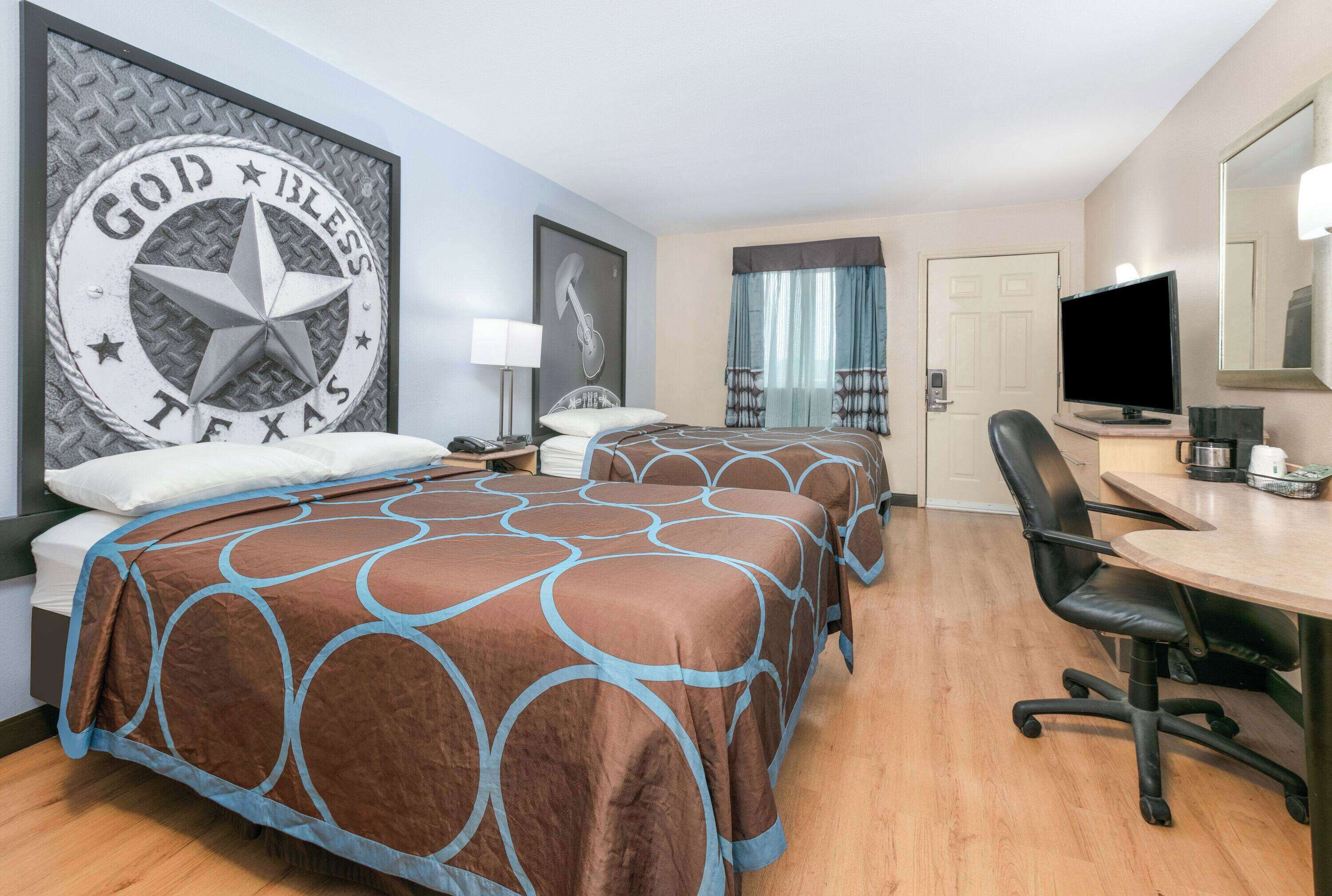 A hotel room with two beds, a desk, a chair, a television, and a framed wall decoration.