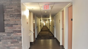 A hotel hallway with a brick accent wall, multiple doors, and an exit sign. - Super 8 by Wyndham New Braunfels I-35 (New Braunfels)