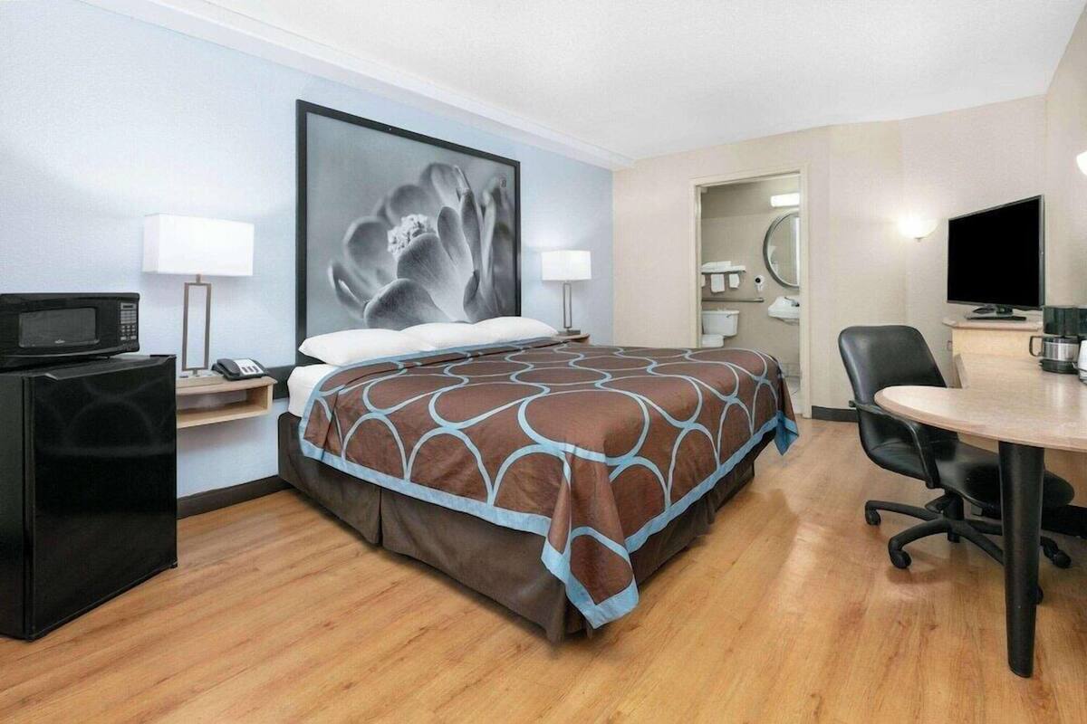 Een hotelkamer met een bed, een bureau, een stoel, een televisie, een magnetron en een badkamer, zichtbaar door een geopende deur.