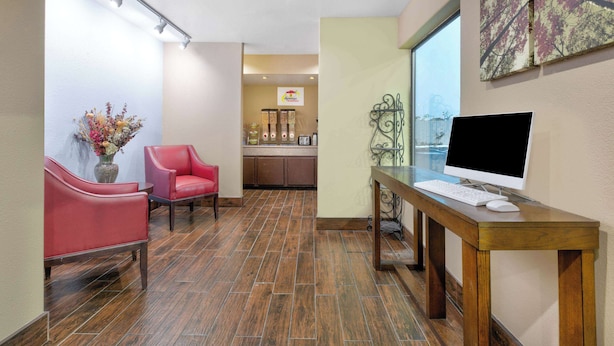 A reception area with a wooden desk, a computer, a red chair, and a vase of flowers. - Super 8 by Wyndham New Braunfels I-35 (New Braunfels)