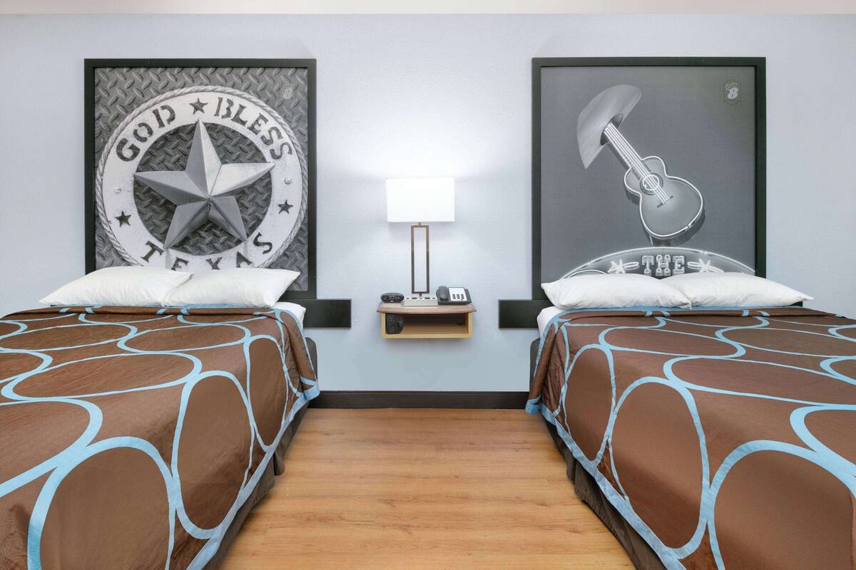 Een hotelkamer met twee bedden, een nachtkastje met een lamp en twee ingelijste foto's aan de muur.