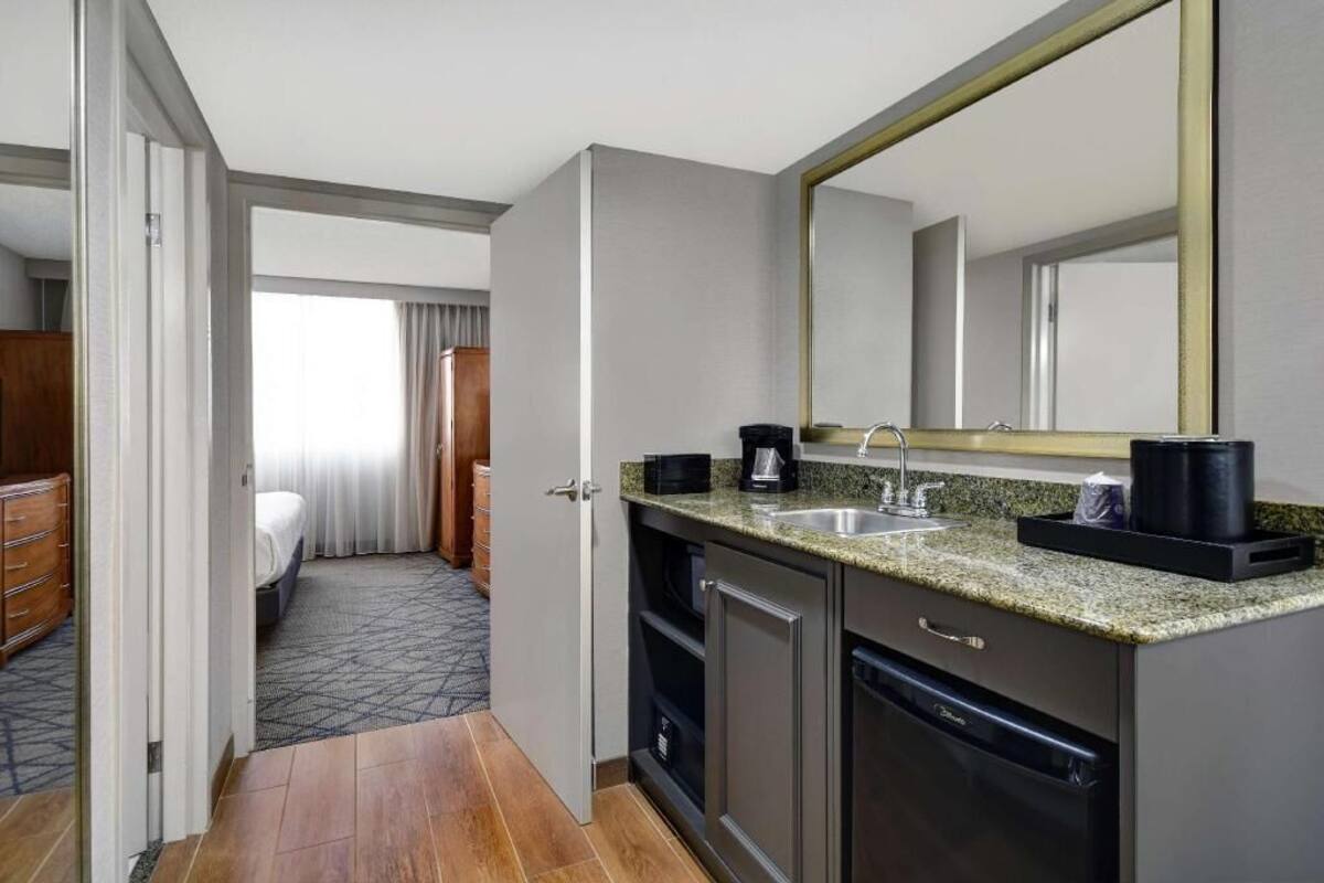Ein Hotelzimmer mit Küchenzeile, einem großen Spiegel, einem Bett und einem Badezimmer.