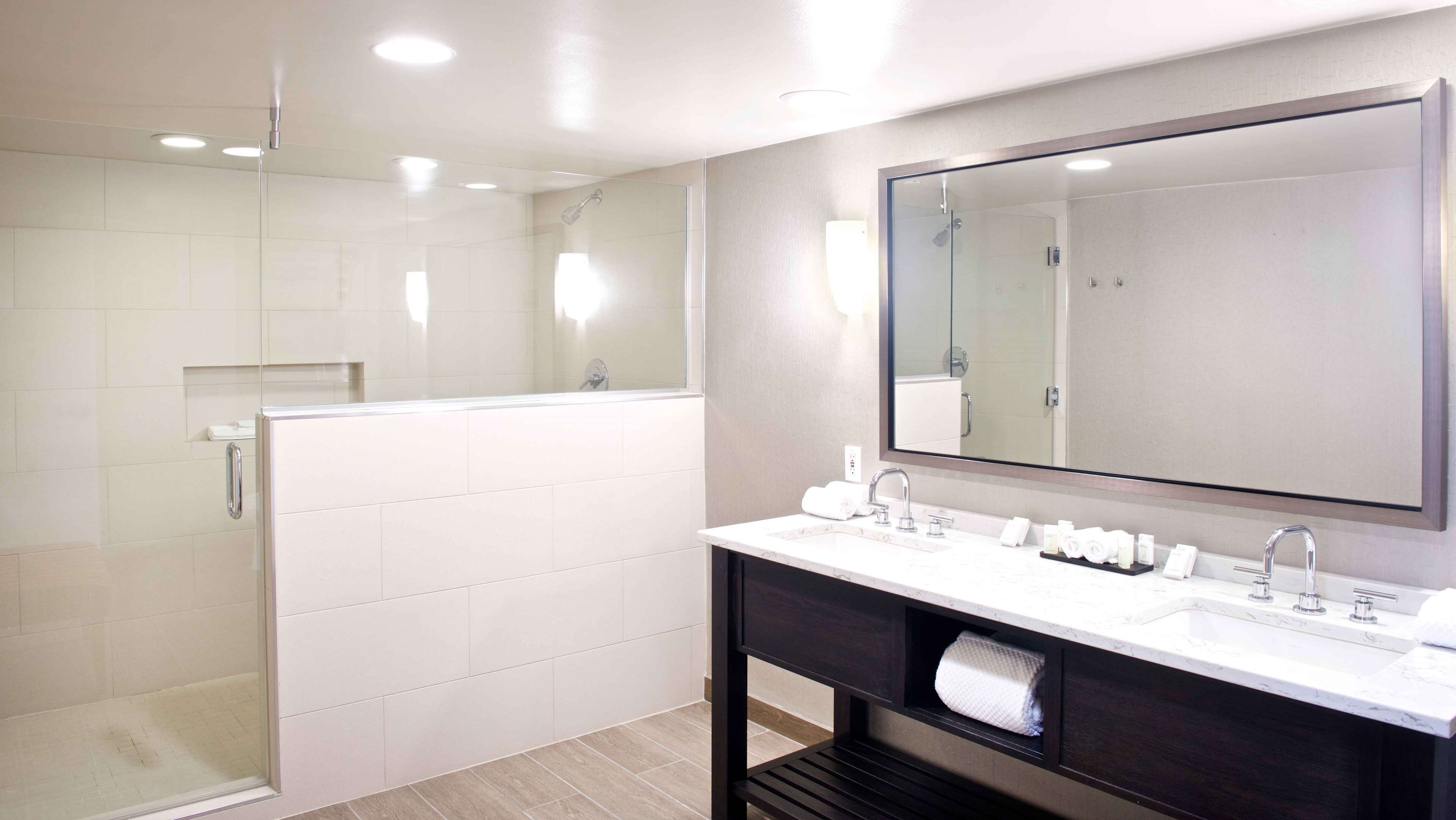 Une salle de bain moderne avec une douche à parois de verre, un grand miroir et un meuble-lavabo doté d’un évier et d’un porte-serviettes.