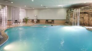 A large indoor pool with a waterfall feature, seating areas, and a view of a rocky wall. - Embassy Suites by Hilton Detroit Livonia Novi (Livonia)