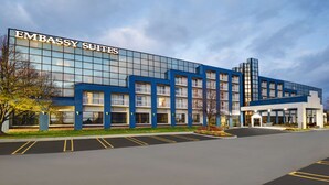 A modern building with a sign reading "Embassy Suites". It features a glass facade, multiple balconies, and a parking lot. - Embassy Suites by Hilton Detroit Livonia Novi (Livonia)
