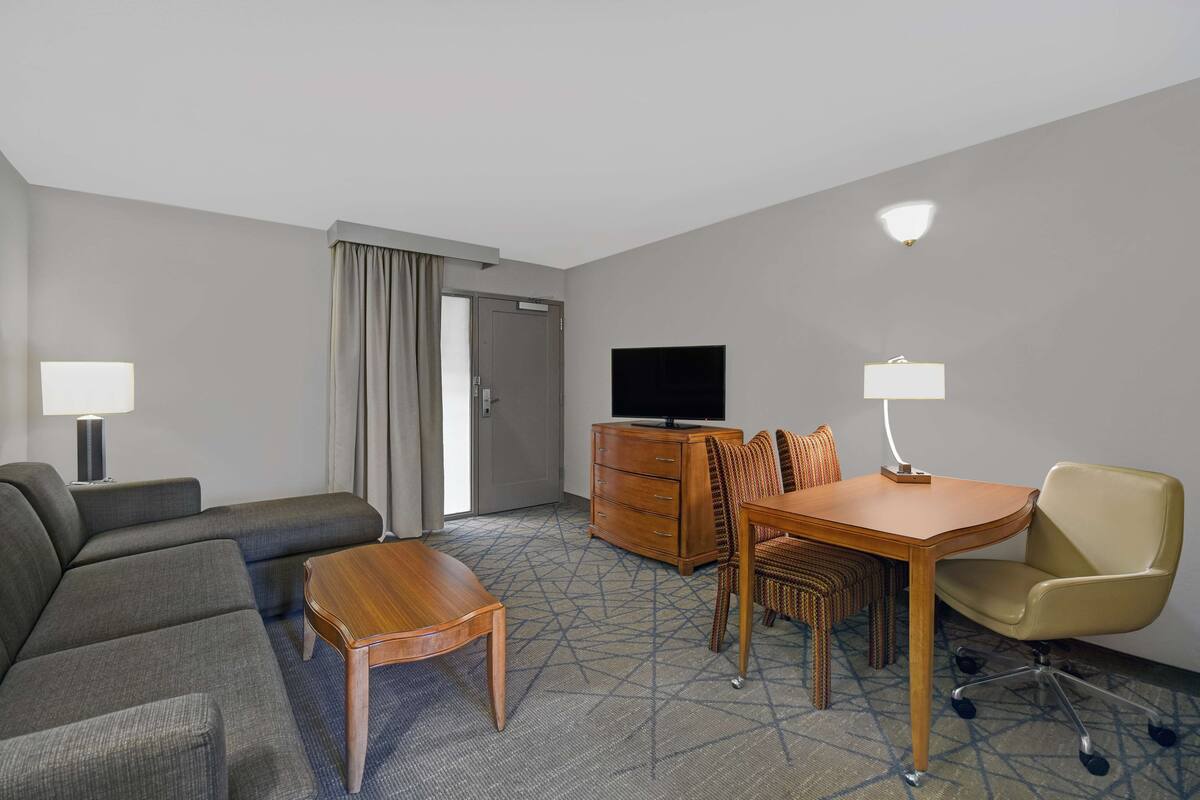 Ein Hotelzimmer mit einer Couch, einem Holztisch, einem Fernseher, einem Schminktisch und einem Sessel.
