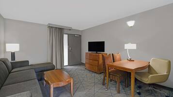 Una habitación de hotel con sofá, una mesa de madera, televisión, cómoda y una silla.