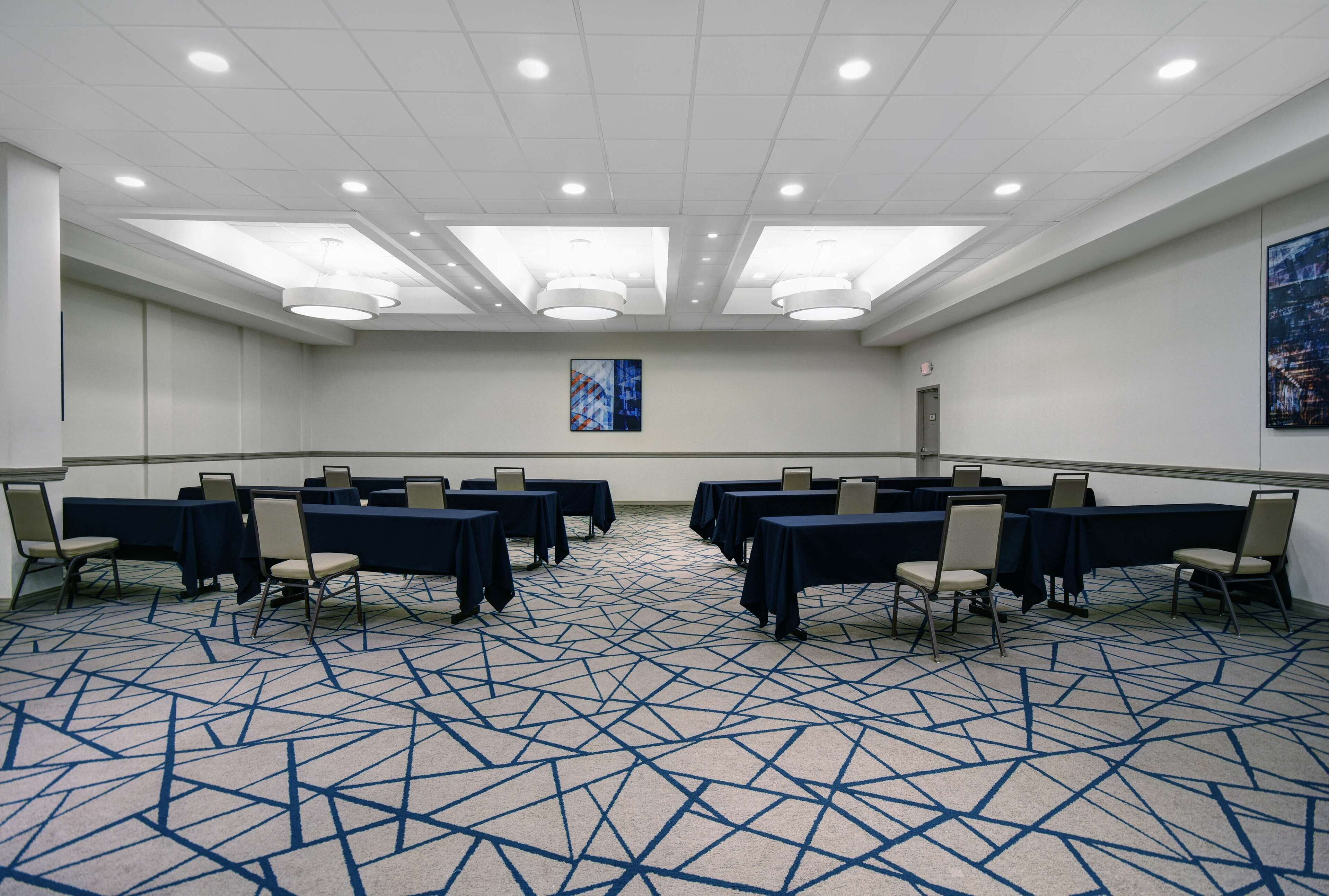 A conference room with tables and chairs, a patterned carpet, and a ceiling with recessed lighting.