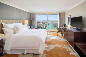 Habitación de hotel con una cama grande, televisión, escritorio y vista a la ciudad.