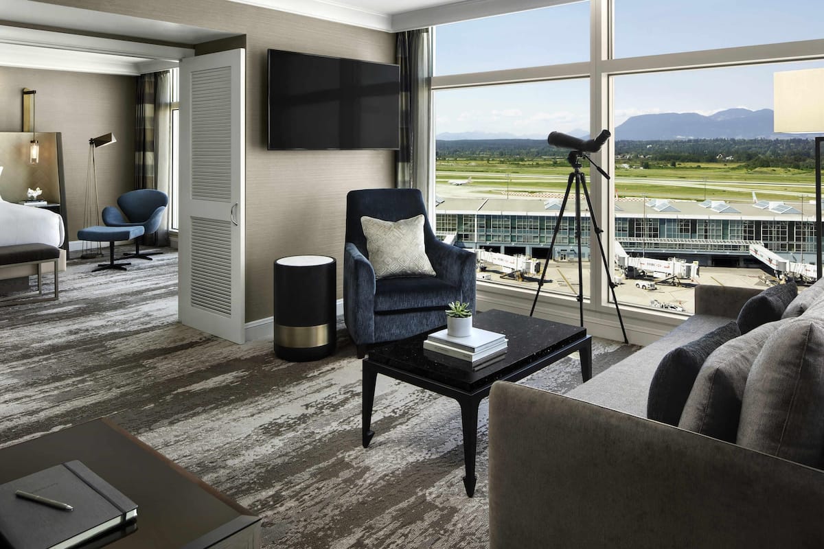 Hotelkamer met een groot raam, een flatscreen-tv, een bureau met lamp, een stoel en een bank.