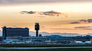 An airport terminal with a control tower, multiple hangars, and parked aircraft.