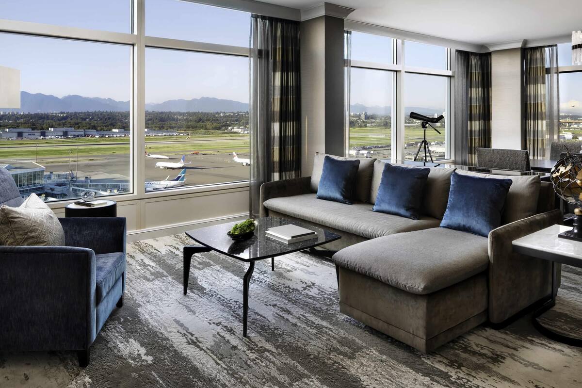 Een moderne hotelkamer met een groot raam dat uitzicht biedt op een vliegveld en bergen.