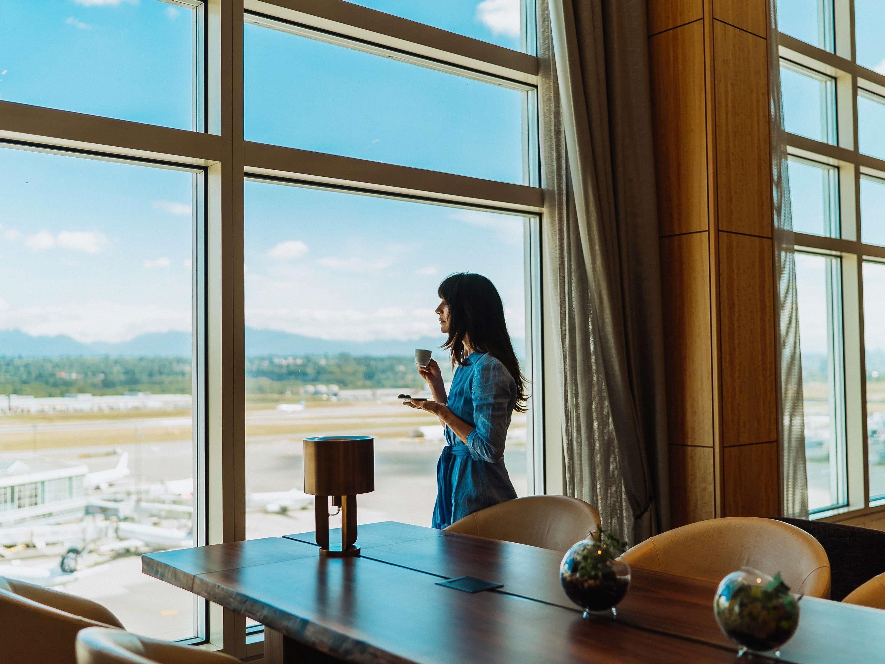 A room with large windows, a wooden table, and a view of an airport.