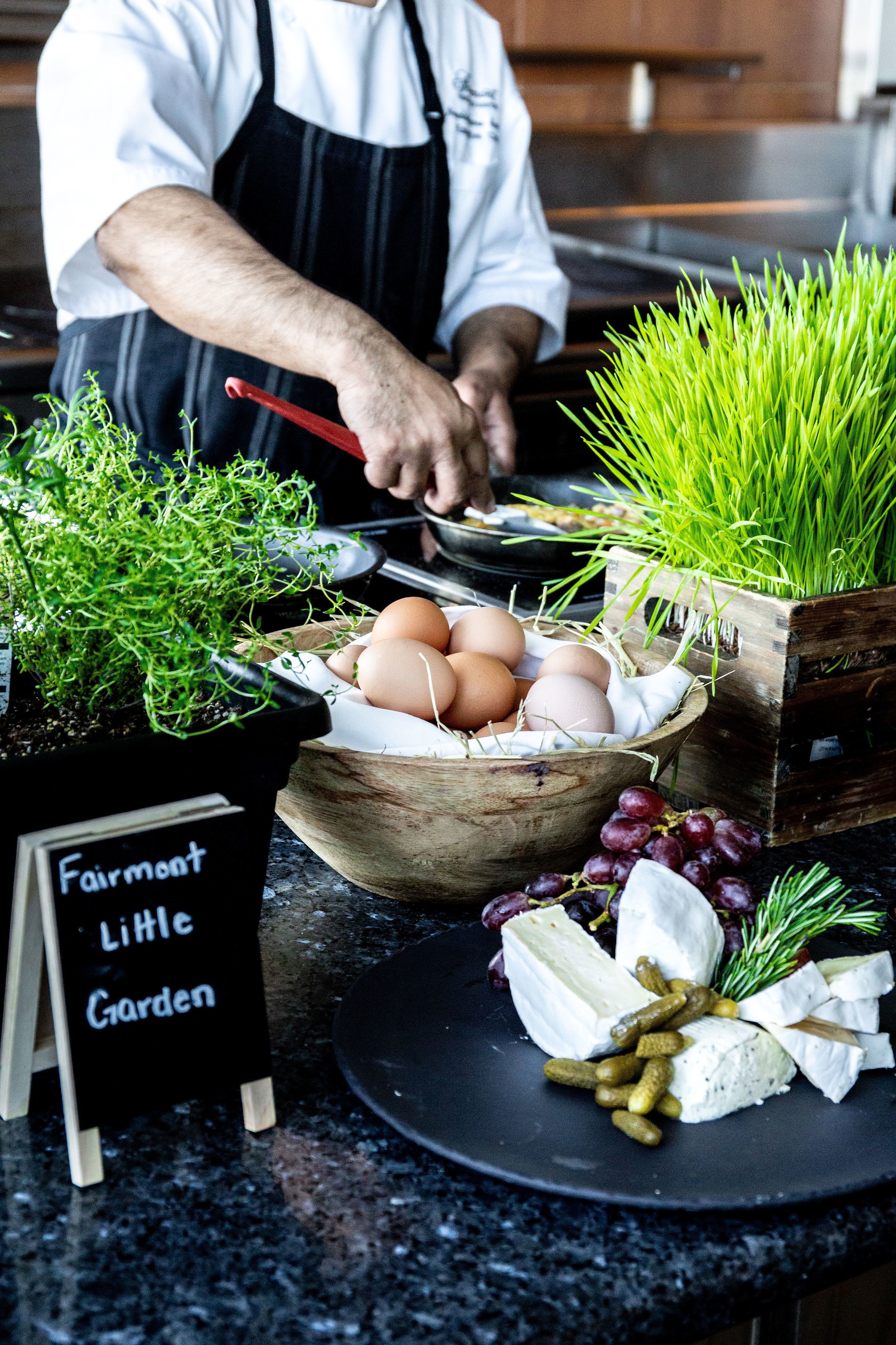 Un chef prépare un plat à base d’œufs, de légumes verts et de fromage sur un plan de travail de cuisine.