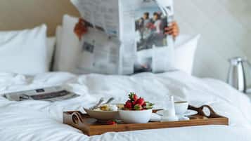 A hotel room with a bed, a tray with breakfast items, and a person reading a newspaper.