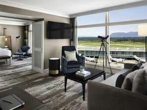 Et hotelværelse med et stort vindue, et fladskærms-tv, et skrivebord med lampe, en stol og en sofa.
