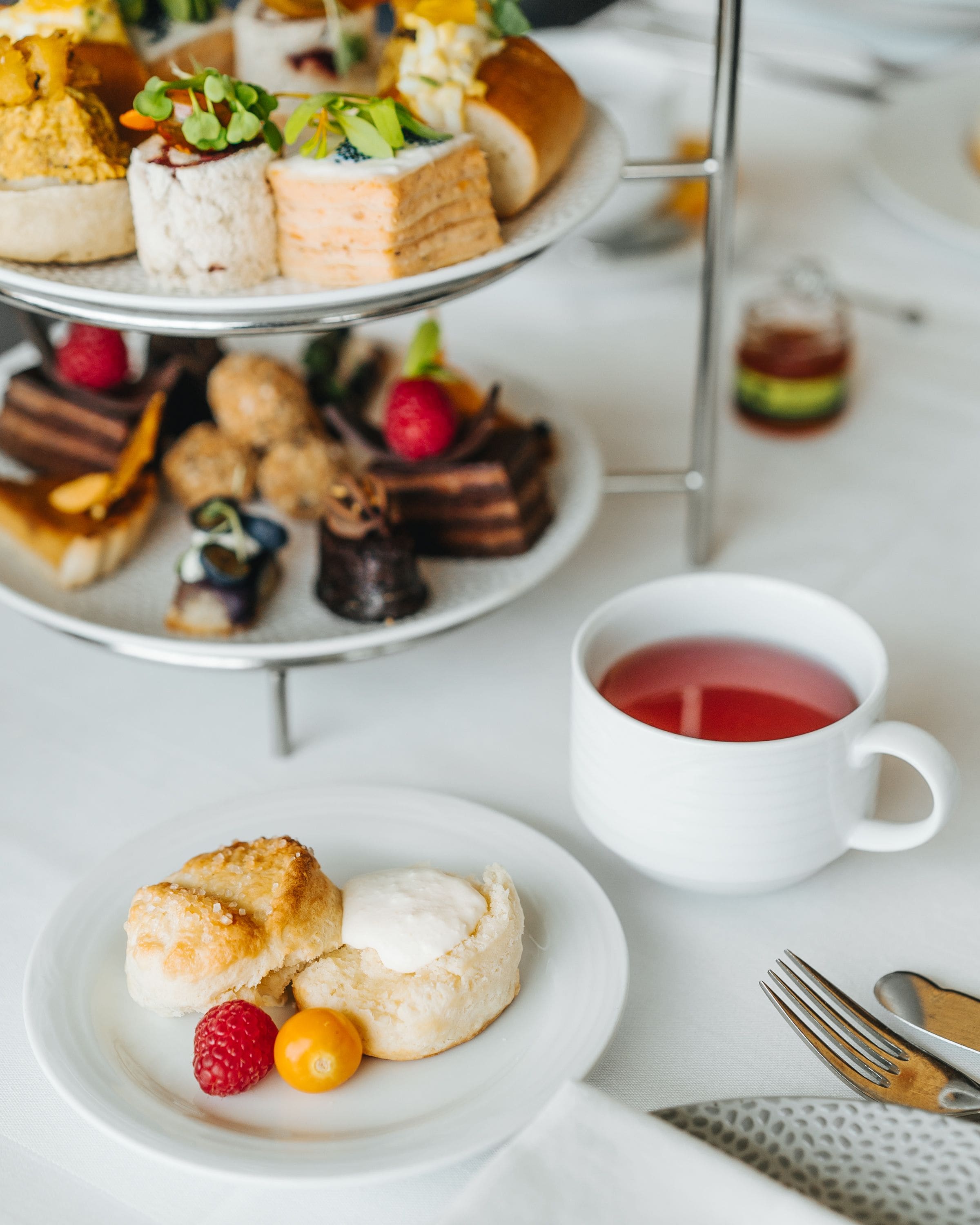 A tiered dessert display with various pastries and a cup of tea on a white table.