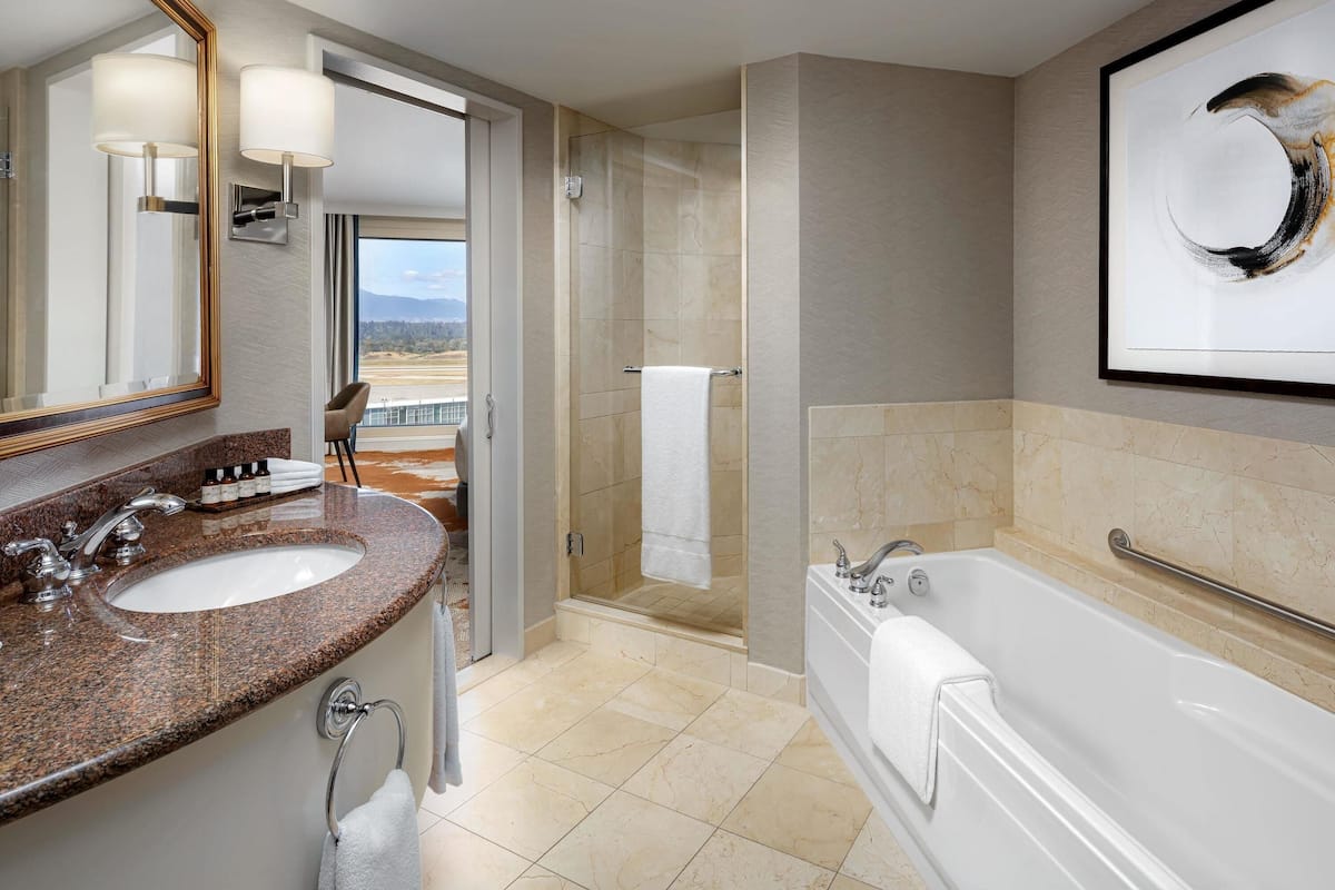 Een moderne badkamer met een wastafel met een granieten blad, een grote spiegel, een badkuip en een douche.