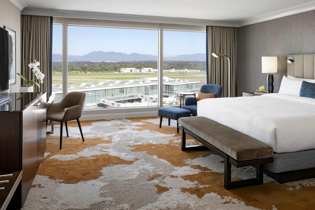 Een hotelkamer met een groot raam, een bed, een bureau, een stoel en een bank.