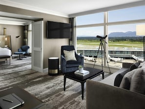 A hotel room with a large window, a flat-screen TV, a desk with a lamp, a chair, and a sofa. - Fairmont Vancouver Airport In-Terminal Hotel (Richmond)