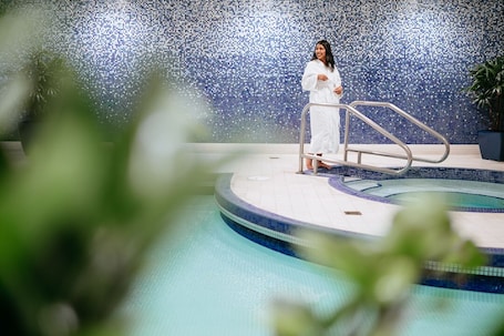 A person standing by a pool with a tiled mosaic wall in the background.