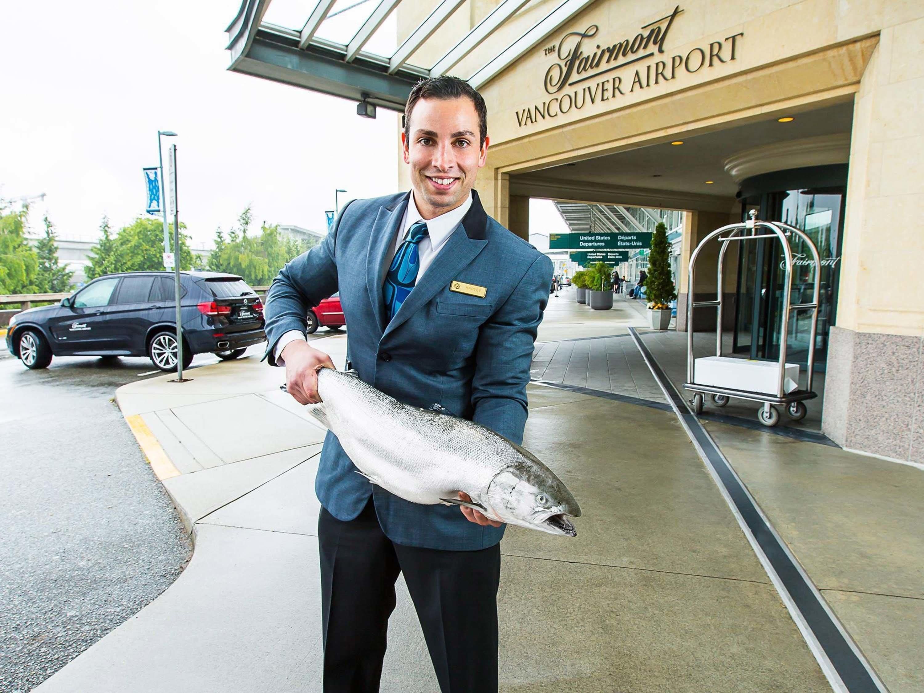 A man holding a fish in front of The Fairmont Vancouver Airport.
