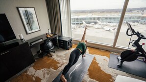 Una habitación con un ventanal grande que da a un aeropuerto, una cinta de correr y una colchoneta para yoga en el suelo.