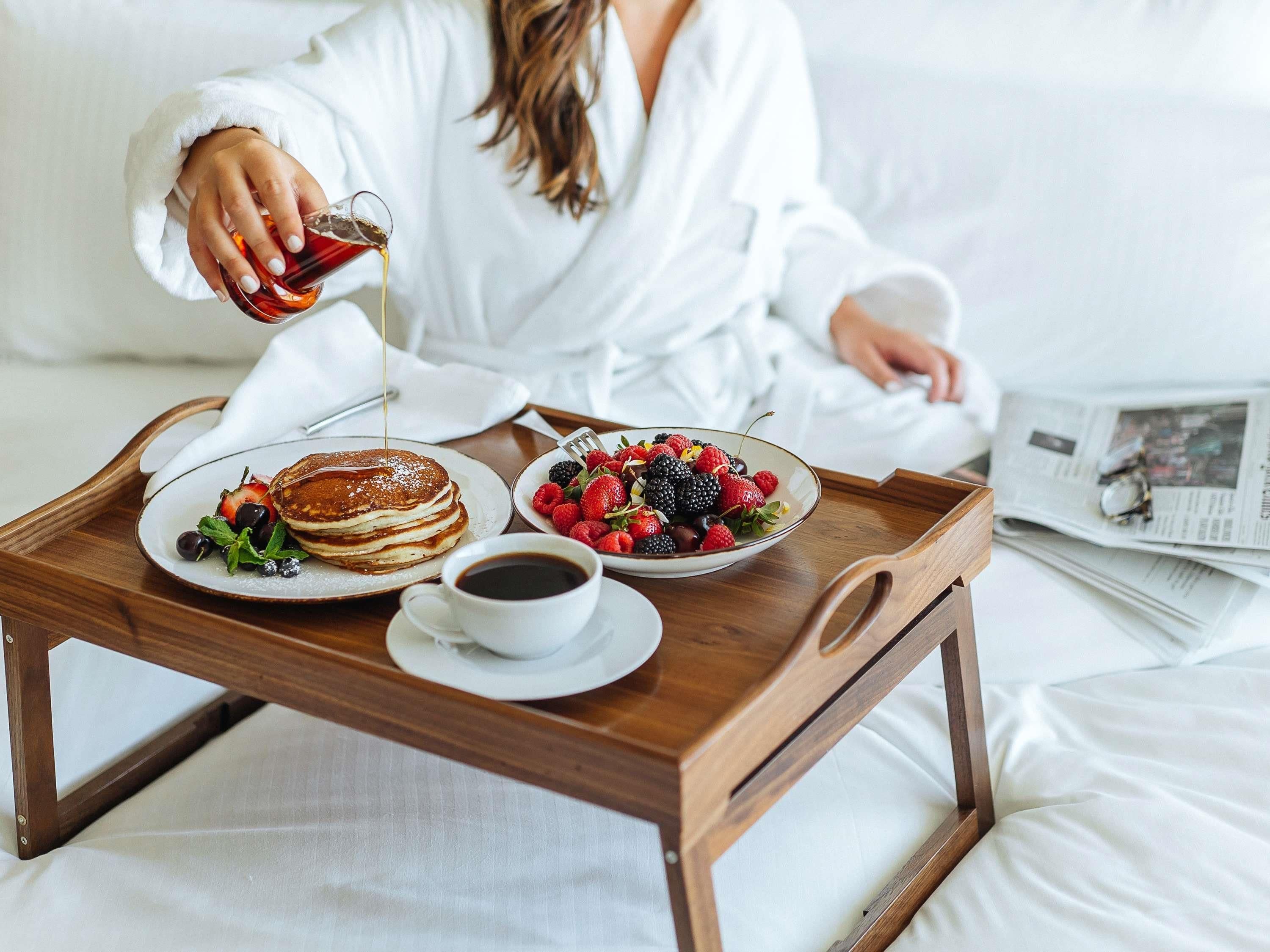A breakfast tray with pancakes, coffee, and a fruit bowl on a bed.