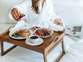 Bandeja de desayuno con panqueques, café y un bol de fruta sobre la cama.